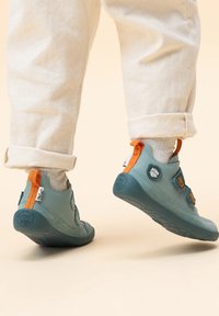 Scarpe flessibili grigio-blu con accenti arancioni, dotate di cinturini con chiusura a strappo, punta arrotondata e suole in gomma testurizzata.
