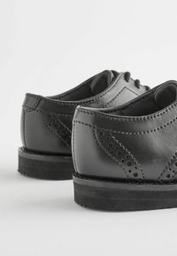 Chaussures en cuir noir avec des orteils arrondis, des détails perforés et des semelles en caoutchouc basses. Surface lisse avec des coutures contrastées.