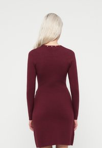 Bordo haljina dugih rukava s uskim krojem, glatkom teksturom i pet dekorativnih dugmadi na stražnjem izrezu.