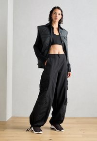 Svarta cargobyxor med sidofickor, en kort svart topp och en ärmlös vadderad svart väst. Har en avslappnad passform och texturerad yta.