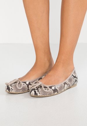 Pies que llevan zapatos de ballet planos con patrón de piel de serpiente beige y negro y un pequeño lazo anudado en la parte superior.
