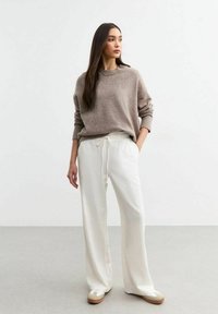 Suéter de punto marrón claro con puños acanalados, combinado con pantalones anchos blancos con cinturilla ajustable. Tejido ligero y corte relajado.