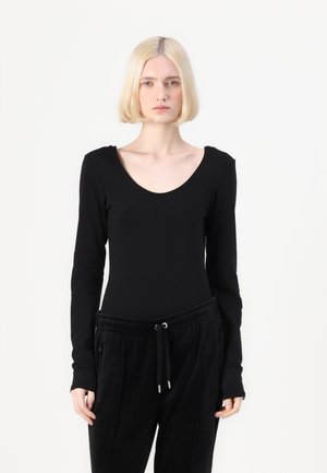 Schwarzes langärmliges Body mit Rundhalsausschnitt, kombiniert mit schwarzen Jogginghosen mit Kordelzug und seitlichen Taschen. Sanfte Textur.
