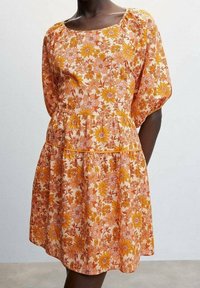 Robe florale avec des manches courtes à volants, ornée d'un motif de fleurs orange et roses sur un fond pêche clair, avec une taille froncée.