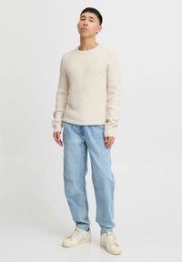 Crème ribgebreide trui met lange mouwen, gecombineerd met lichtblauwe, loszittende jeans en beige sneakers. Eenvoudig ontwerp, geen patronen.
