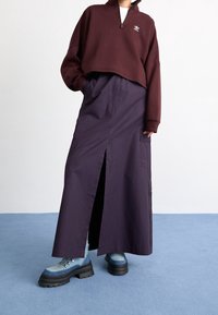 Bourgogne kort sweatshirt med halvmidja, logotypdetalj, tillsammans med en lång, djup blå kjol med en framfåra och sidofickor. Tjocka blå stövlar.