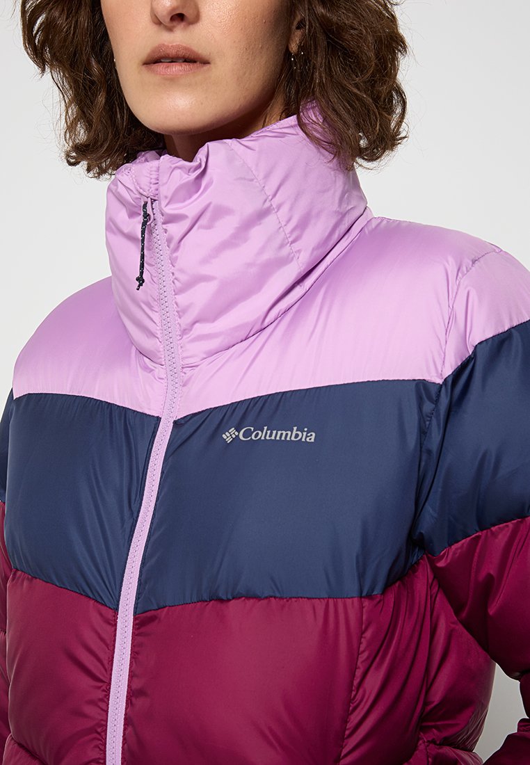 Chaqueta tipo puffa con un alto cuello, diseño en bloques de color en lavanda, azul marino y burdeos, con un logo visible y cremallera en contraste.