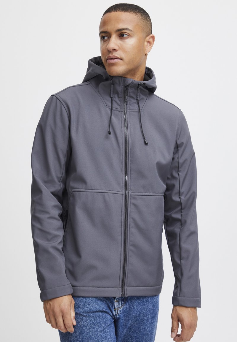 Jachetă gri cu glugă, realizată din material softshell, având fermoar complet, șnururi ajustabile și buzunare laterale. Croială casual cu o textură netedă.