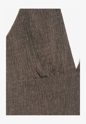 Nærbillede af brunt stof med et tekstureret gittermønster og en V-udskæring med subtile rynker ved brystområdet.