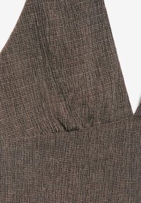 Close-up van bruin stof met een textuur van geruit patroon en een V-hals met subtiele plooien bij het borstgedeelte.