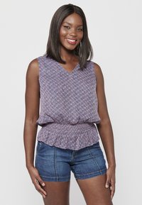 Mouwloze top met bloemenpatroon, een V-hals en een peplum taille; gemaakt van een lichte stof in tinten paars en roze. Draagt met denim shorts.