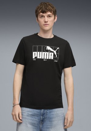 Juodas medvilninis marškinėliai su apvaliu iškirpimu, su baltu Puma logotipu ir tekstu stačiakampio formos grafiniame dizaine. Trumpomis rankovėmis.