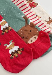 Drie paar sokken: rood met rendieren, groen met sneeuwvlokken, tan gestreept met rendieren; allemaal met een zachte gebreide textuur en speelse patronen.