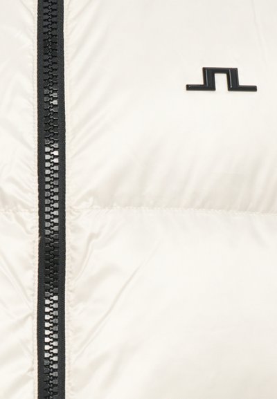 Cream-colored puffer jacket featuring a black zipper, black logo accent, and a smooth, glossy texture with piped seams.