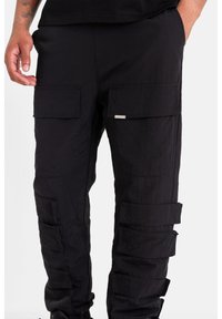 Černé cargo kalhoty z lehké, texturované tkaniny. Obsahují několik velkých kapes a nastavitelná poutka po stranách.