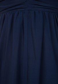 Tissu bleu foncé avec des plis froncés et une couture qui descend verticalement au centre.