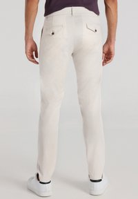 Chinos de color claro hechos de una tela suave, que presentan bolsillos traseros con acentos de botón y un corte ajustado. Llevados con zapatillas blancas.