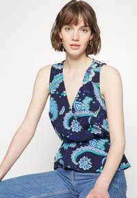 Top em florais azul-marinho com padrões paisley em azul-turquesa e branco. Apresenta um decote profundo em V, design sem mangas e uma cintura franzida.