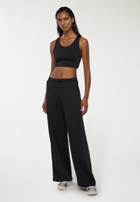 Czarny krótki top na ramiączkach w połączeniu z luźnymi czarnymi spodniami dresowymi. Materiał wydaje się gładki, z elastycznym paskiem w talii i detalami w postaci troczka.