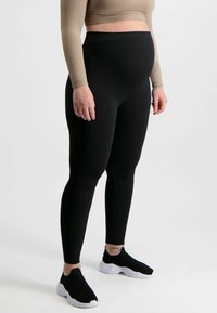 Zwarte geribde legging met een hoge tailleband, gemaakt van rekbaar materiaal, gecombineerd met zwarte instapschoenen en een contrasterend beige cropped top.