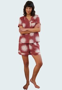 Red short-sleeve pajama set featuring sun patterns in cream, with a button-up top and matching shorts, made from lightweight fabric.