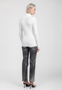 Maglia bianca a maniche lunghe con colletto alto, abbinata a pantaloni metallici argento slim-fit. L'outfit presenta dettagli sartoriali e una vestibilità strutturata.