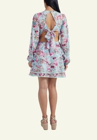 Floral dress with long sleeves, open back with a bow detail, layered ruffle hem, and a light blue background. Worn with strappy wedge shoes.