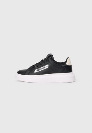Baskets basses noires avec semelle épaisse blanche et languette beige au talon, avec le logo "Just Cavalli" sur le côté et des lacets noirs.