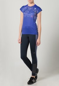 Blue athletic shirt with cap sleeves and abstract pattern, paired with dark leggings featuring gray stripes and fitted design.