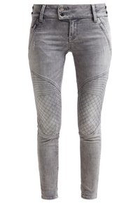 Jeans skinny de denim gris con parches acolchados en las rodillas, un acabado desgastado y detalle de cintura con doble botón. La textura es suave con un ligero desgaste.