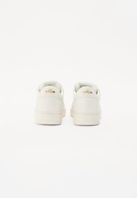 Hvide lædersneakers med en glat tekstur, rund form og tanfarvede gummisåler. Gyldne accenter på hælen tilføjer en særprægede detalje.