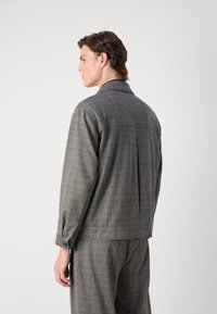 Grau karierter Blazer mit entspannter Passform, ausgestattet mit einem Kragen, knöpfbaren Manschetten und einer Falte auf der Rückseite für zusätzlichen Bewegungsfreiheit.