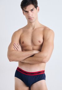 Temno modri moški bokserice iz mehkega blaga z rdečim elastičnim pasom, na katerem je logotip "HUGO". Preprost dizajn, standardna prileganje.