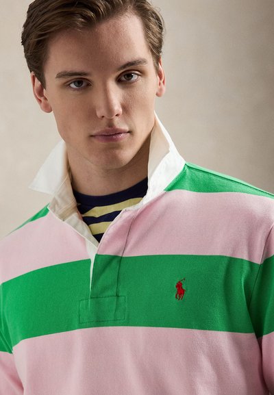 Ριγέ πόλο πουκάμισο με ροζ και πράσινες οριζόντιες ρίγες, λευκό γιακά και μικρό κόκκινο κεντητό λογότυπο στο στήθος.