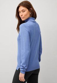 Blauwe turtleneck trui van zachte brei, met lange mouwen en een relaxte fit, gecombineerd met zwarte leggings. Eenvoudig en minimalistisch ontwerp.