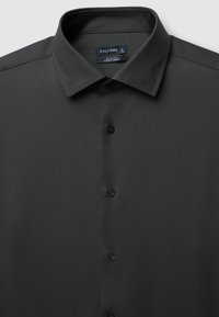Camicia slim-fit, facile da stirare, di colore verde scuro. Presenta un collo classico, bottoni frontali e una consistenza liscia. L'etichetta interna reca la scritta "CALLIOPE," taglia L.