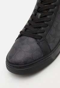 Fekete sneaker, textúrázott bőr felsőrésszel, geometrikus mintázattal, kerek orral és lapos fűzőkkel, mindez gumi talpon.