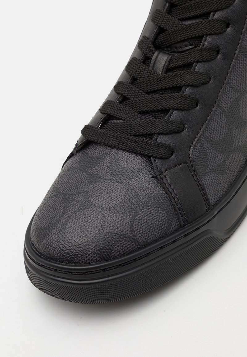 Schwarze Sneaker mit Obermaterial aus strukturiertem Leder und geometrischem Muster, runder Zehenform und flachen Schnürsenkeln, alles auf einer Gummisohle.