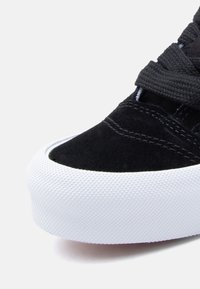 Μαύρο σουέντ αθλητικό παπούτσι με υφασμένη λευκή καουτσούκ σόλα, με στρογγυλεμένη μύτη και καθαρές ραφές στην επάνω πλευρά.