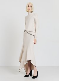 Hellbeiger Strickpullover mit hohem Kragen, kombiniert mit einem passenden Rock mit welligem Saum und schwarzem Besatz. Dazu schwarze High Heels.