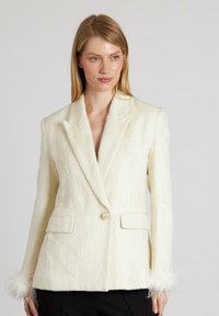 Blazer blanco de lana con solapa muesca, cierre de botón de perla, dos bolsillos frontales y detalles de plumas en los puños. Tejido texturizado.