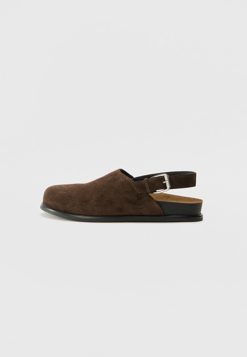 Brown suede slip-on shoe with a low heel, an adjustable strap with a silver buckle, and a black rubber sole.