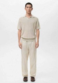 Beżowa dzianinowa koszulka polo z krótkim kołnierzykiem, zestawiona z kremowymi spodniami o szerokich nogawkach i brązowymi, wiązanymi butami. Gładka tekstura, minimalistyczny design.