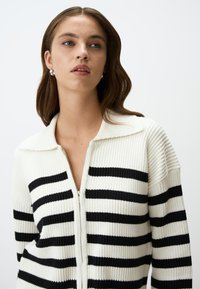 Cardigan zip-up a righe in crema e nero, con texture a coste, un ampio colletto e righe alternate spesse e sottili.
