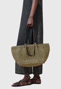 Borsa a tracolla in paglia intrecciata nei toni del nero e del naturale, con manici in pelle nera. Forma rotonda e spaziosa con una superficie texturizzata.