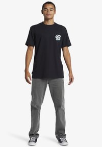 Black cotton t-shirt with front graphic design in light blue. Model wears gray denim pants and black sneakers with white soles.