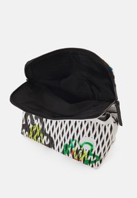 Lukket pung lavet af syntetisk materiale, med en sort inderside, en hvid mesh yderside og et grønt og sort grafisk design.