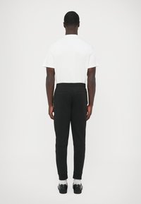 Czarne spodnie dresowe o zwężanym kroju, z elastycznym pasem i ściągaczami przy kostkach. Noszone z prostą białą koszulką.