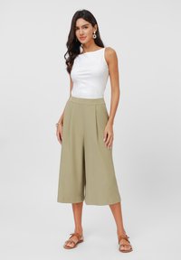 Lehký bílý bezrukávový top, který je zkombinován s khaki culottes s vysokým pasem a plisováním. Výrazné neutrální tóny a ploché hnědé sandály.