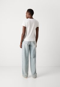 Hvit tettsittende T-skjorte laget av bomull med korte ermer, kombinert med lyseblå, høy midje, vide jeans med synlige sømmer.